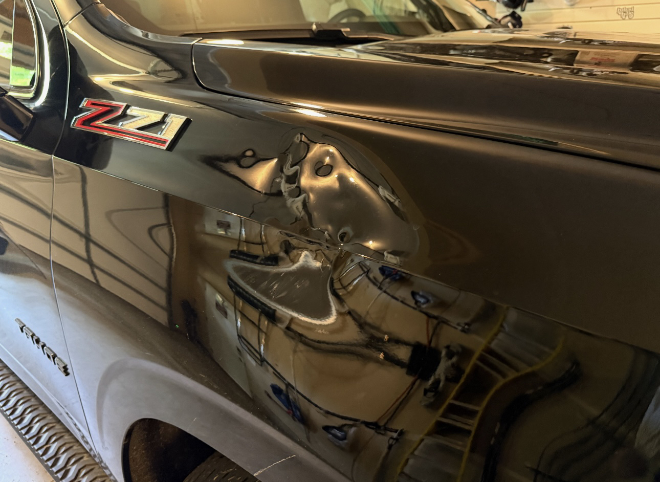 Black Chevrolet Tahoe fender with a large dent before repair